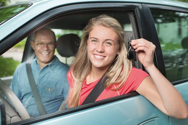 Mädchen hält Schlüssel in die Kamera. Sitzt neben ihrem Fahrlehrer im Auto.