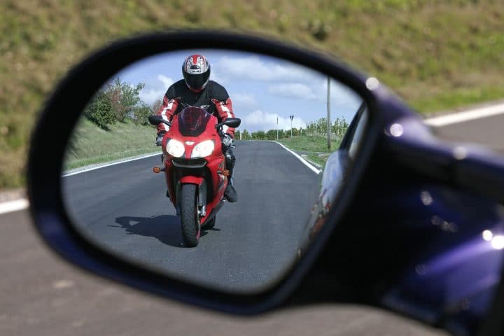 Motorradfahrer nähert sich Auto im Seitenspiegel
