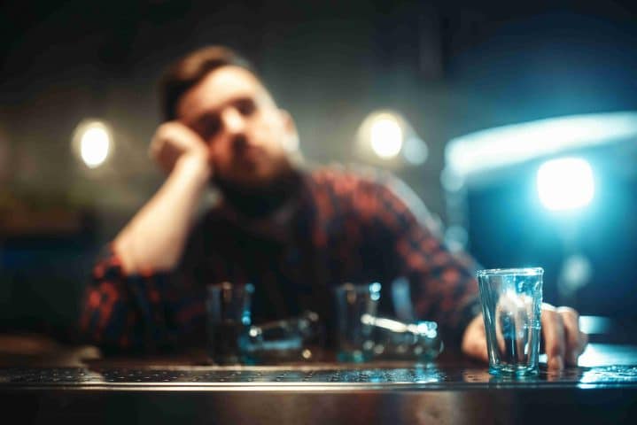 Alkoholisierter Mann sitzt mit Getränk an der Bar.